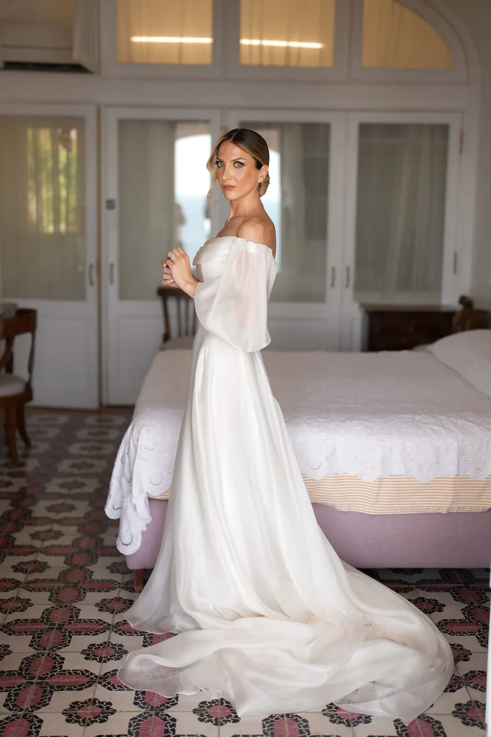 Die Braut im Kleid im Zimmer, die lange Schleppe auf dem Fliesenboden ausgebreitet.