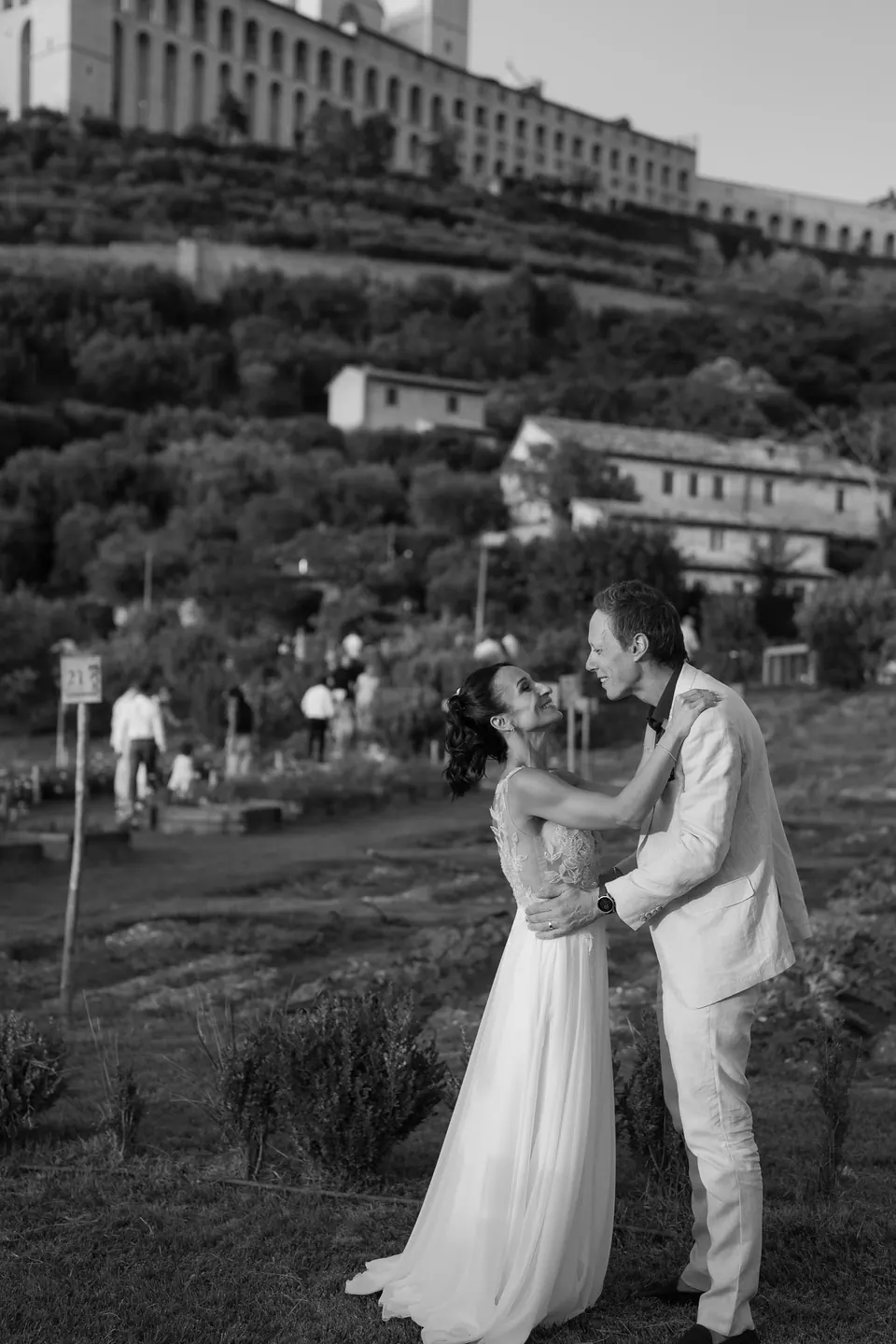 Black and white photo of bride and groom embracing with Assisi behind them