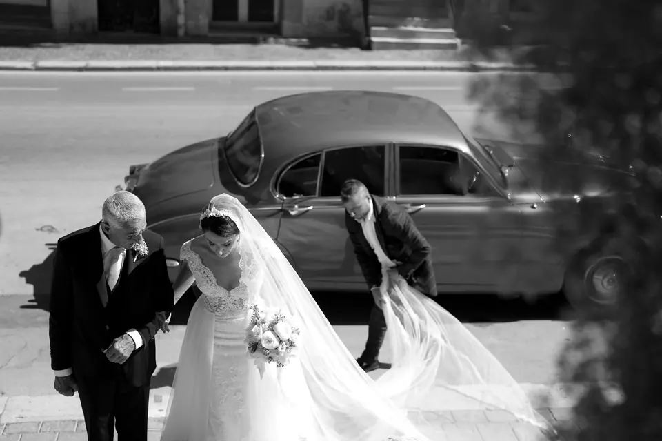 Black and white photo of the bride stepping out of a vintage car with her father