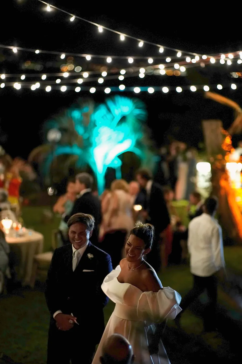 Couple dancing under twinkling lights during the evening reception by the sea.