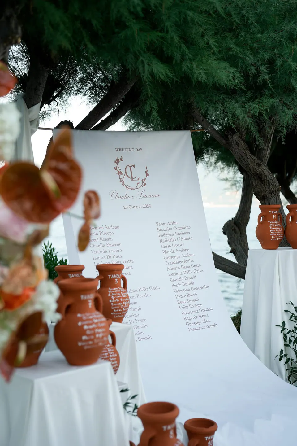 Sitzplan auf weißen Tafeln, dekoriert mit Terrakottakrügen und orangen Blumen.
