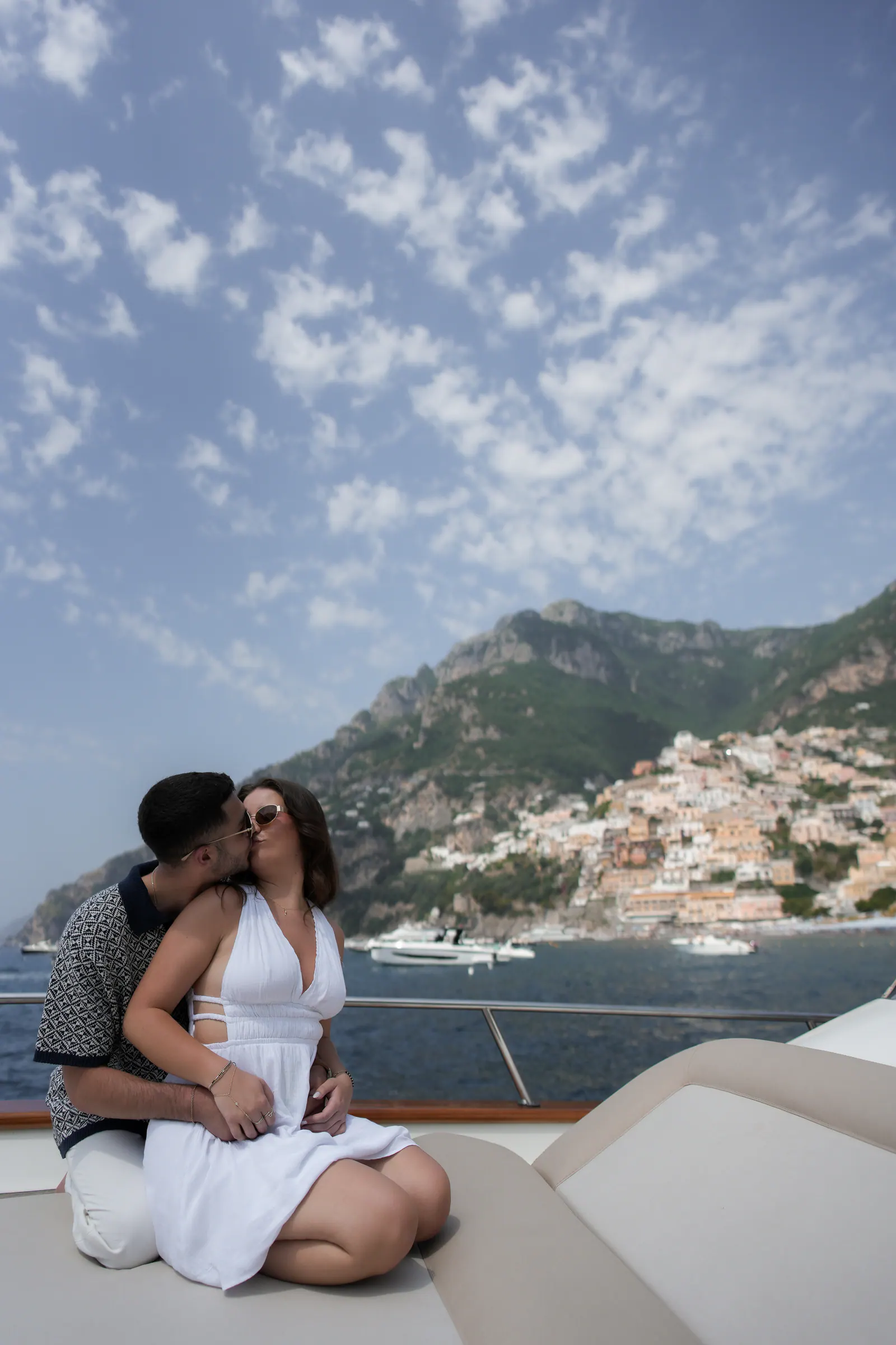 Couple embracing on the bow of a boat, Positano rising behind them.