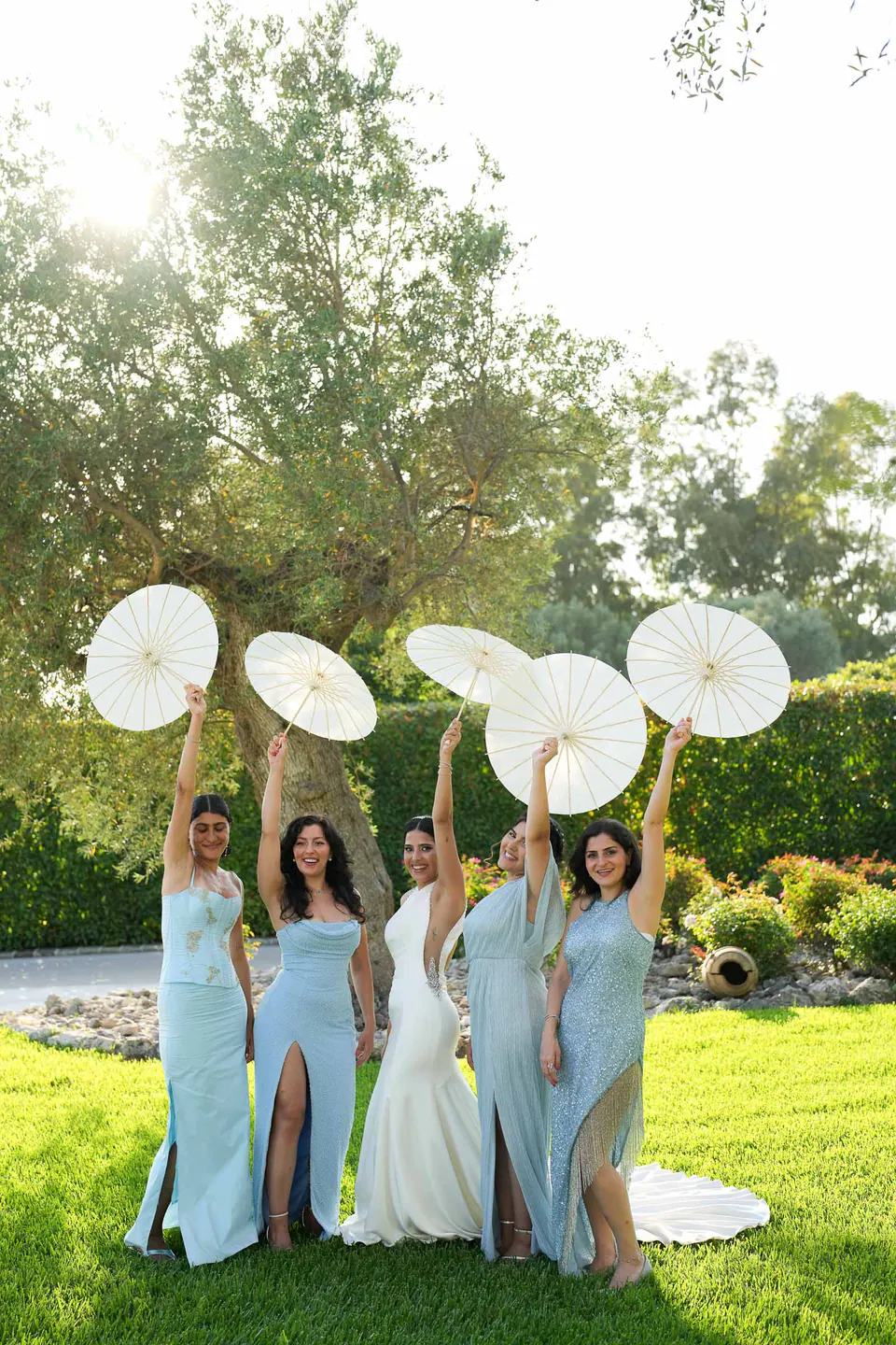 La mariée et ses demoiselles d’honneur en bleu clair lèvent leurs ombrelles en papier vers le soleil.