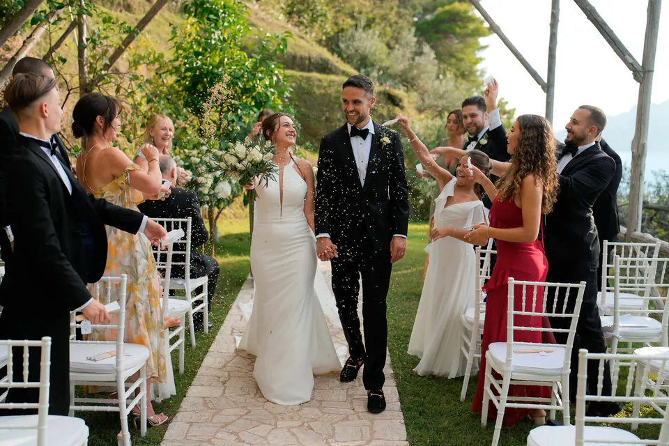 Bride and groom walking back up the aisle as newlyweds between white chairs.