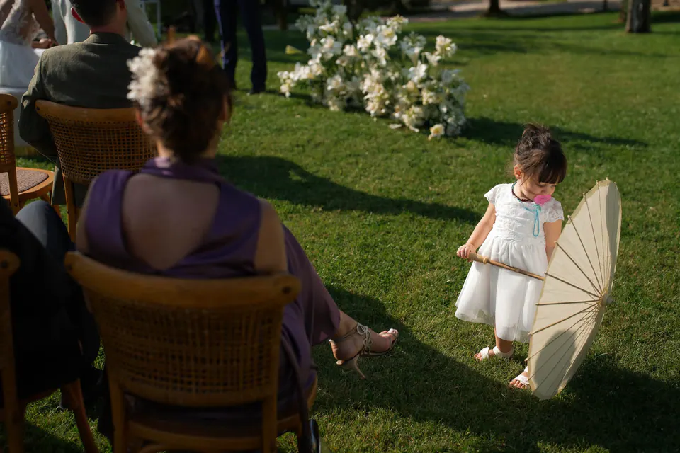 A little girl with a parasol running past a seated guest