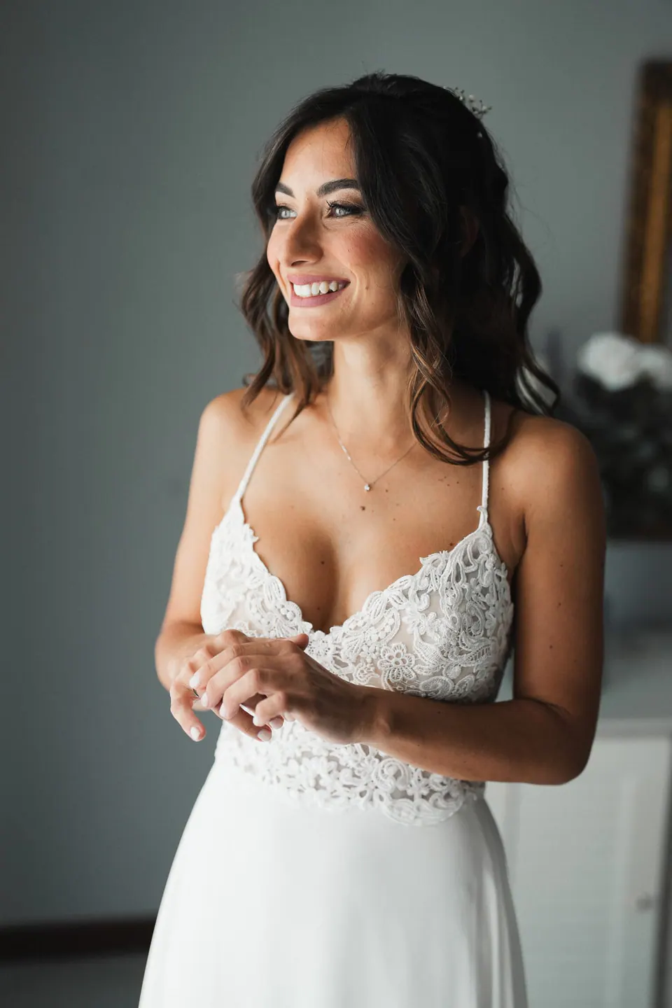 La sposa sorride mentre si prepara, la luce della finestra sul pizzo dell'abito.