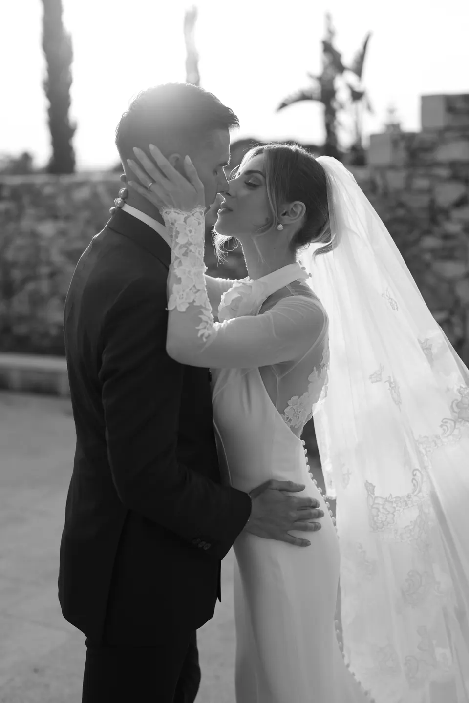 Ritratto in bianco e nero dello sposo che accarezza il viso della sposa mentre lei si avvicina per un bacio.