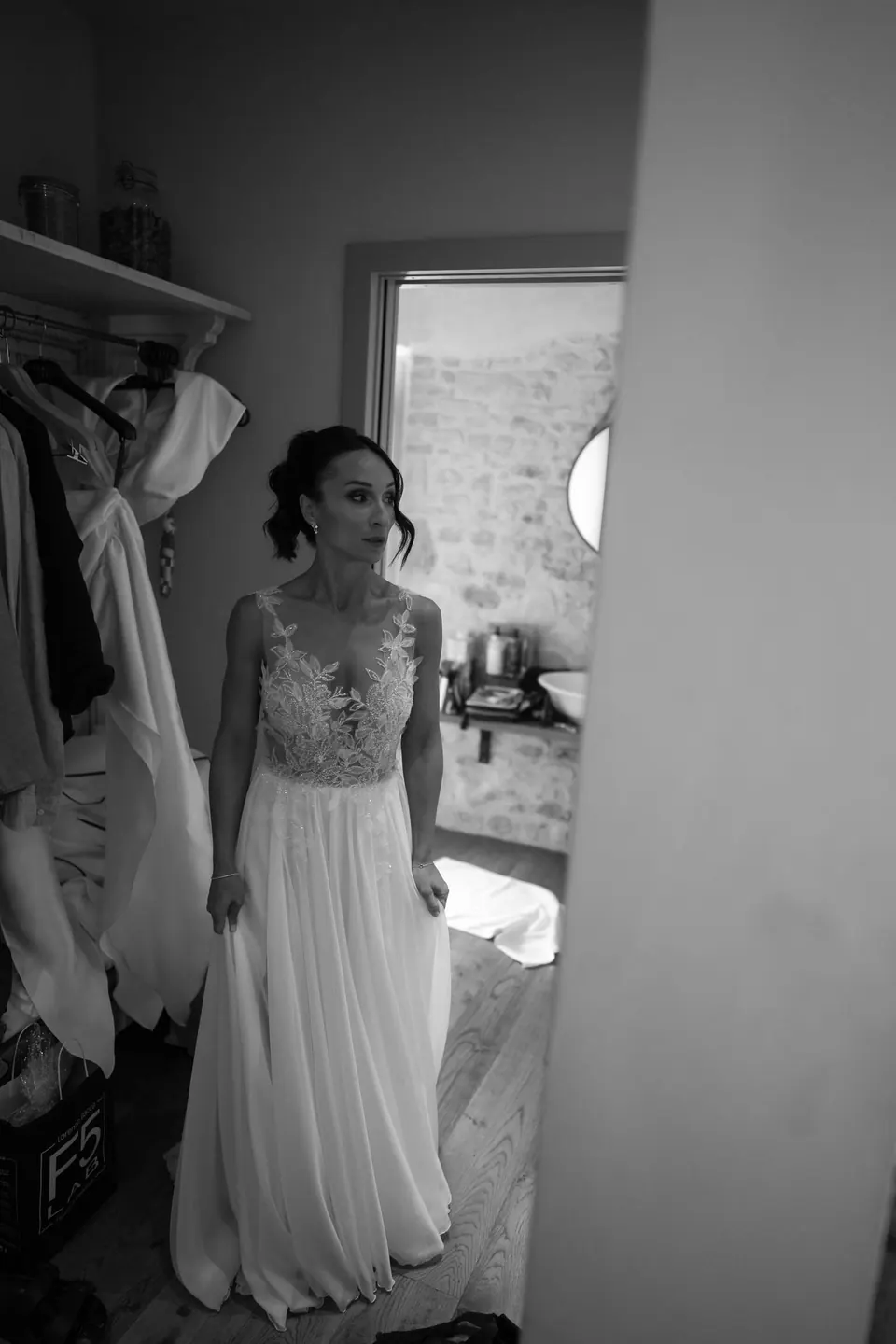 Black and white photo of the bride in her dress by a doorway