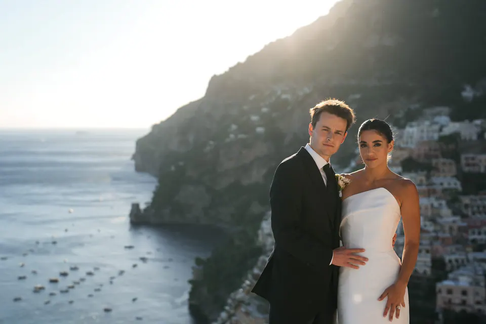 Bride and groom on the terrace, the cliffs of Positano and the sea behind them.