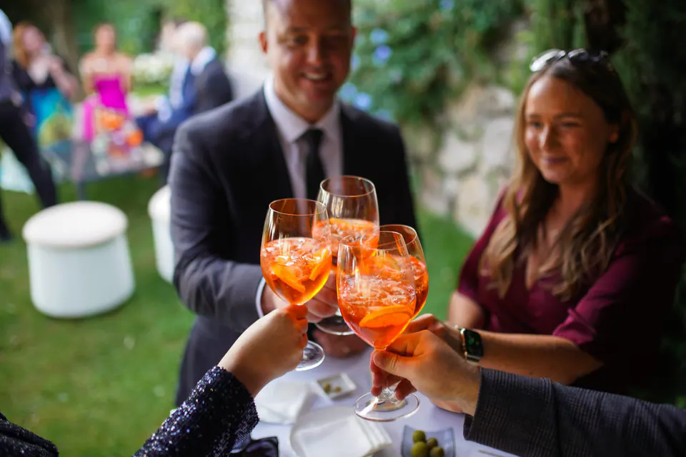 Guests clinking glasses with Aperol Spritz at cocktail hour, vibrant Italian celebration moment.
