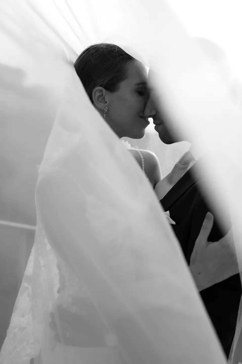 Black and white close-up of the couple under the veil, foreheads touching.